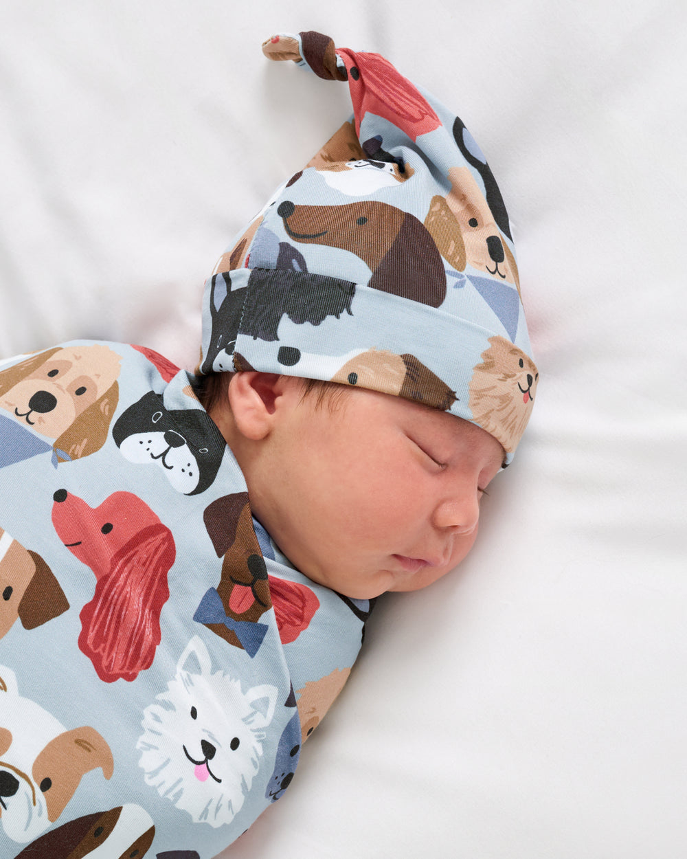 Close up of baby wearing the Gray Puppy Parade Swaddle & Hat Set