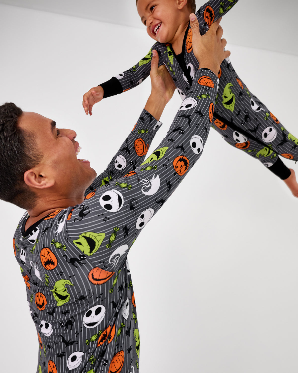 Father holding up child wearing matching Disney The Nightmare Before Christmas pajamas