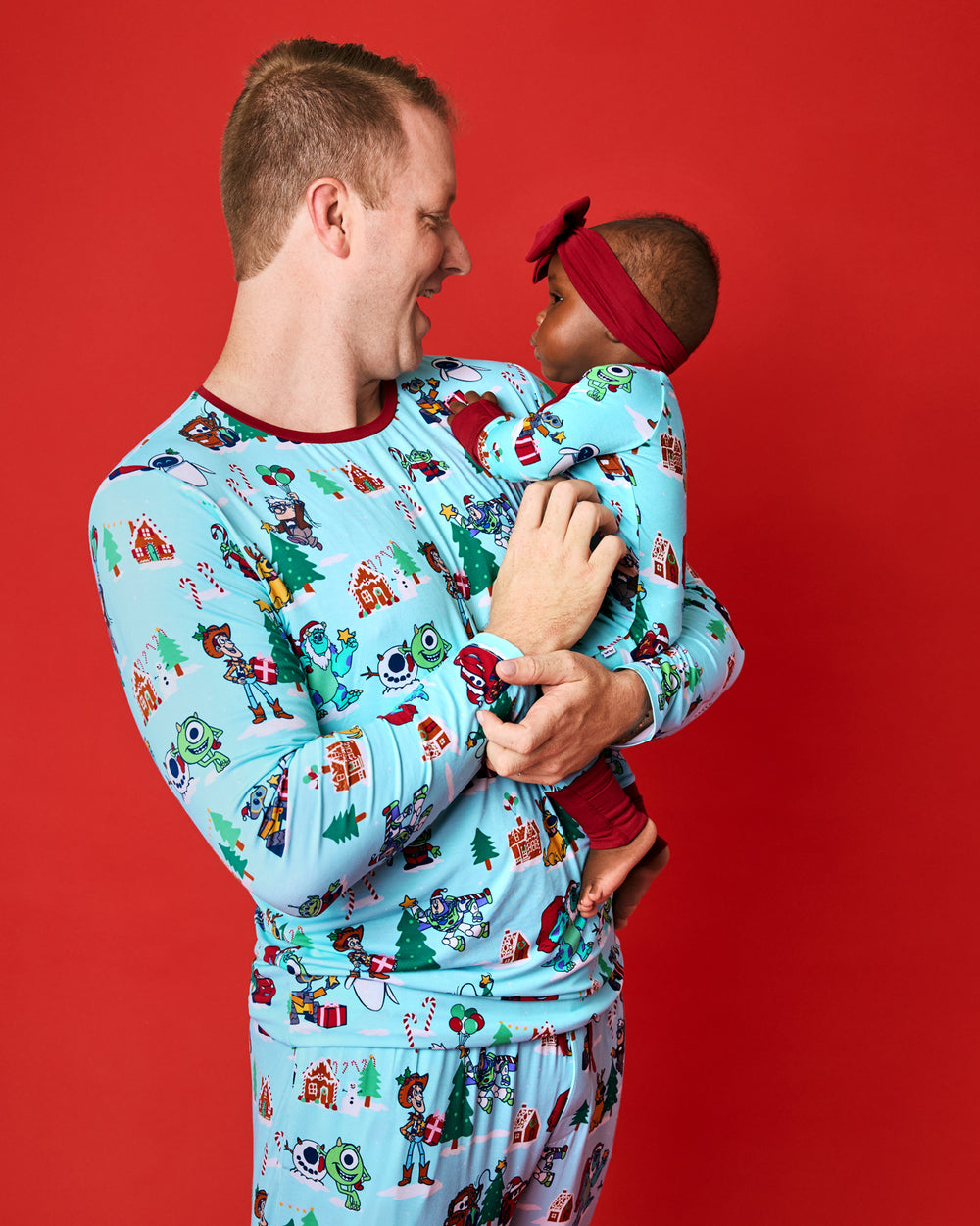 Father and daughter wearing matching Disney Christmas Village PJs on a red background