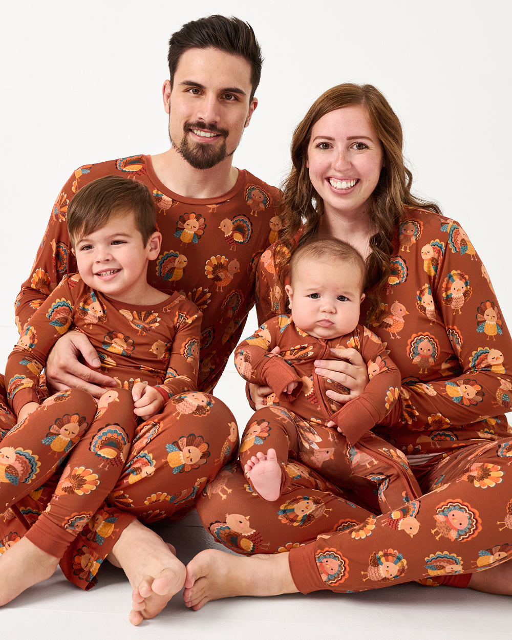 Sitting family of four wearing matching Grateful Gobbles Fall themed pajamas