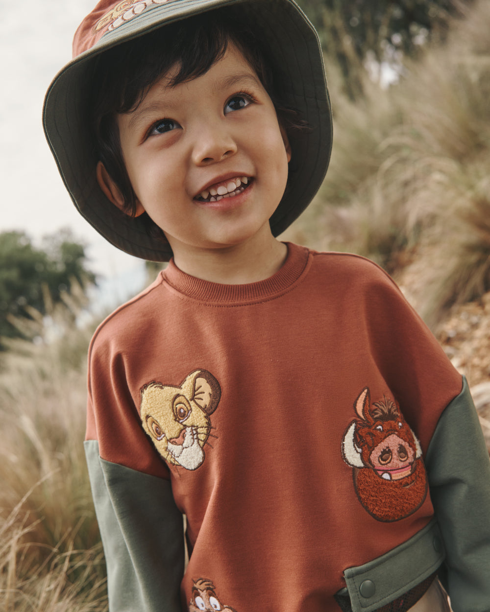 Close up of boy wearing the Disney Jungle Treasures Drop Shoulder Crewneck with a grassy background