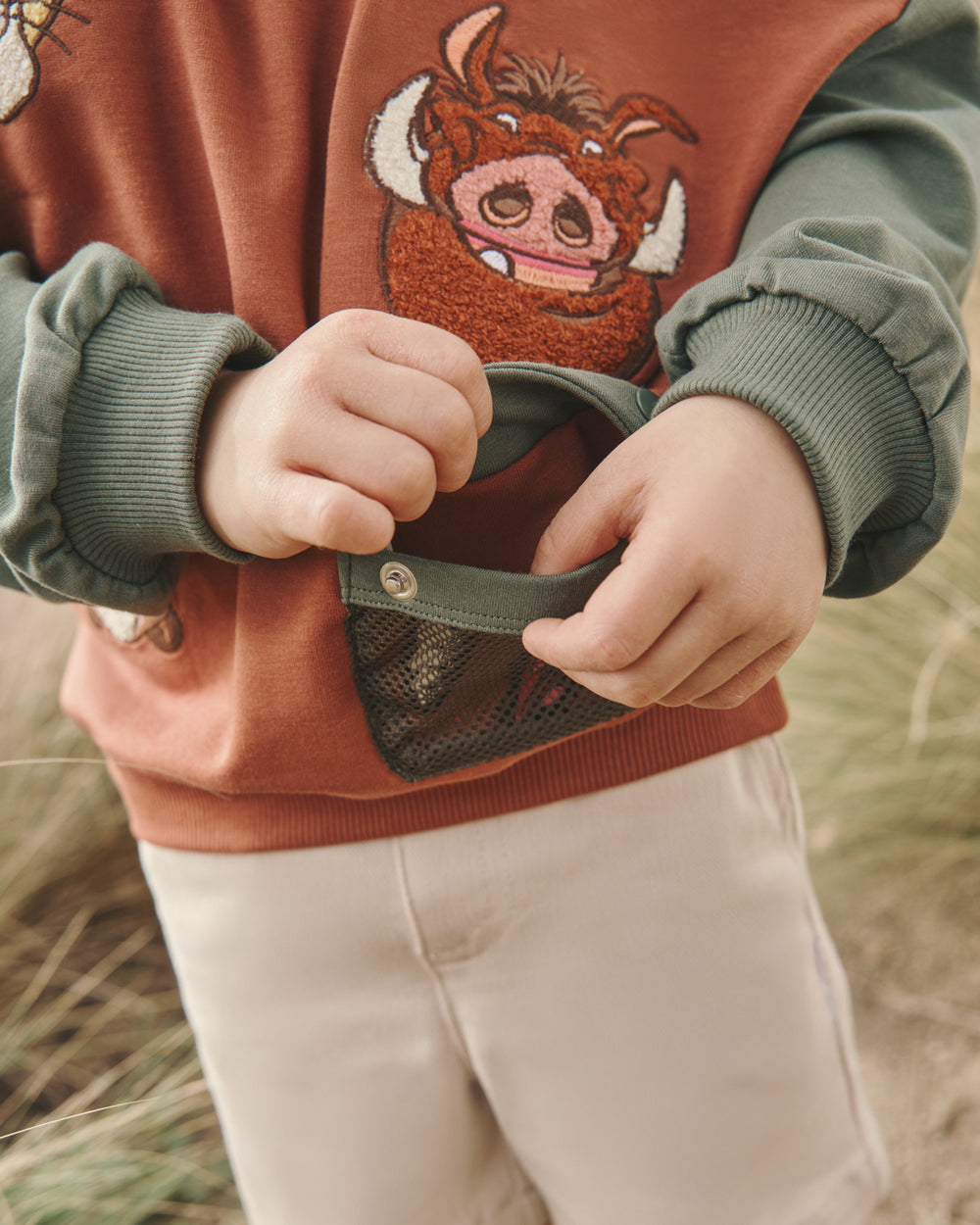 Child demonstrating the pocket feature on the Disney Jungle Treasures Drop Shoulder Crewneck