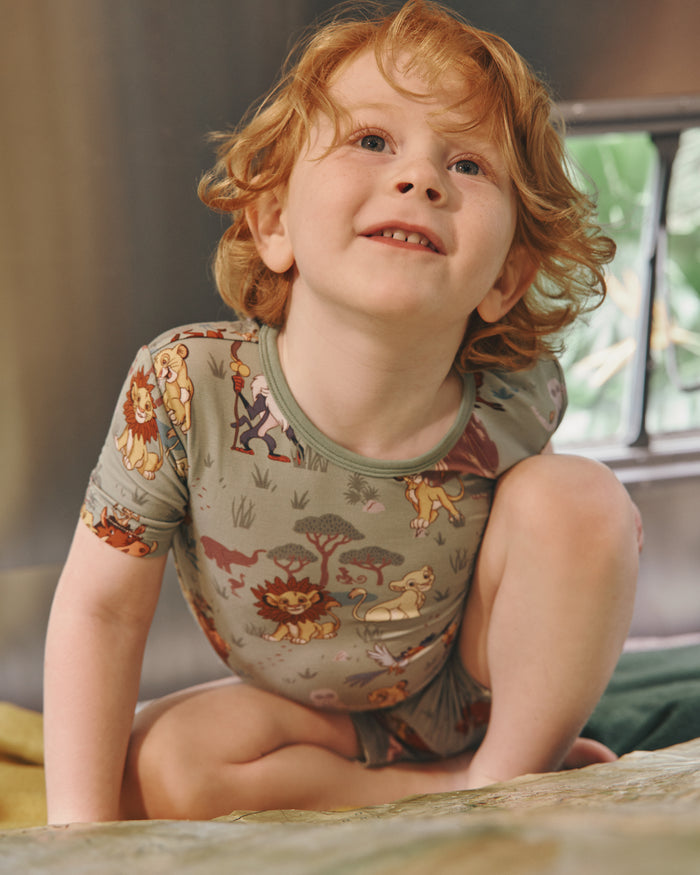 Sitting boy wearing the Disney Simba's Safari Two-Piece Short Sleeve & Shorts Pajama Set in a retro camper