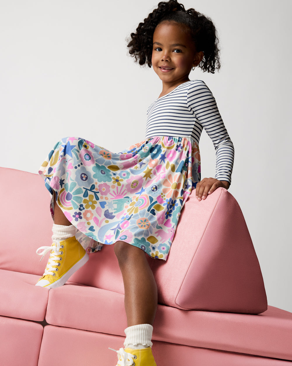 Girl wearing the Unicorn Blossoms Twirl Dress on a pink modular couch