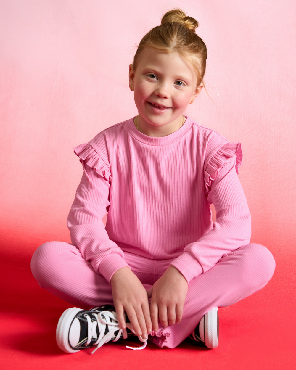 Sitting girl wearing the Sweet Pink Ribbed Flare Pants and Flutter Sweatshirt
