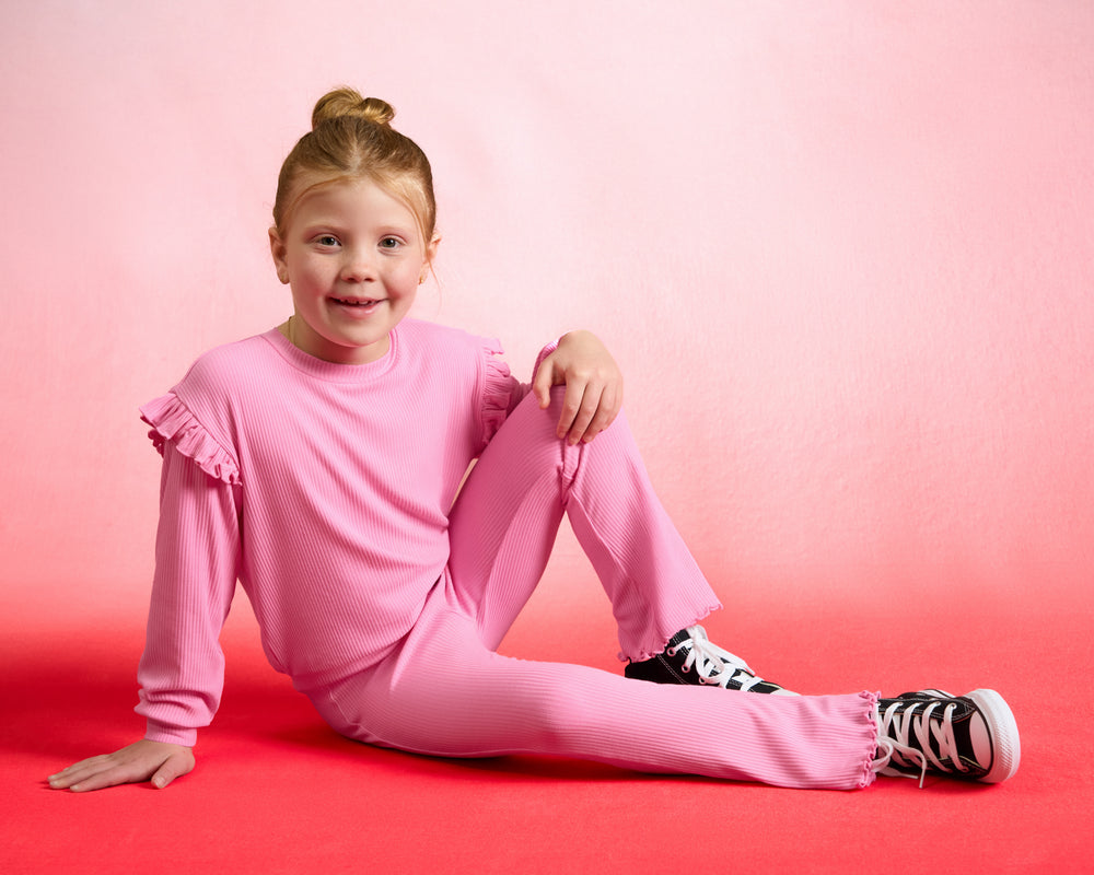 Sitting girl wearing the Sweet Pink Ribbed Flare Pant on a red background