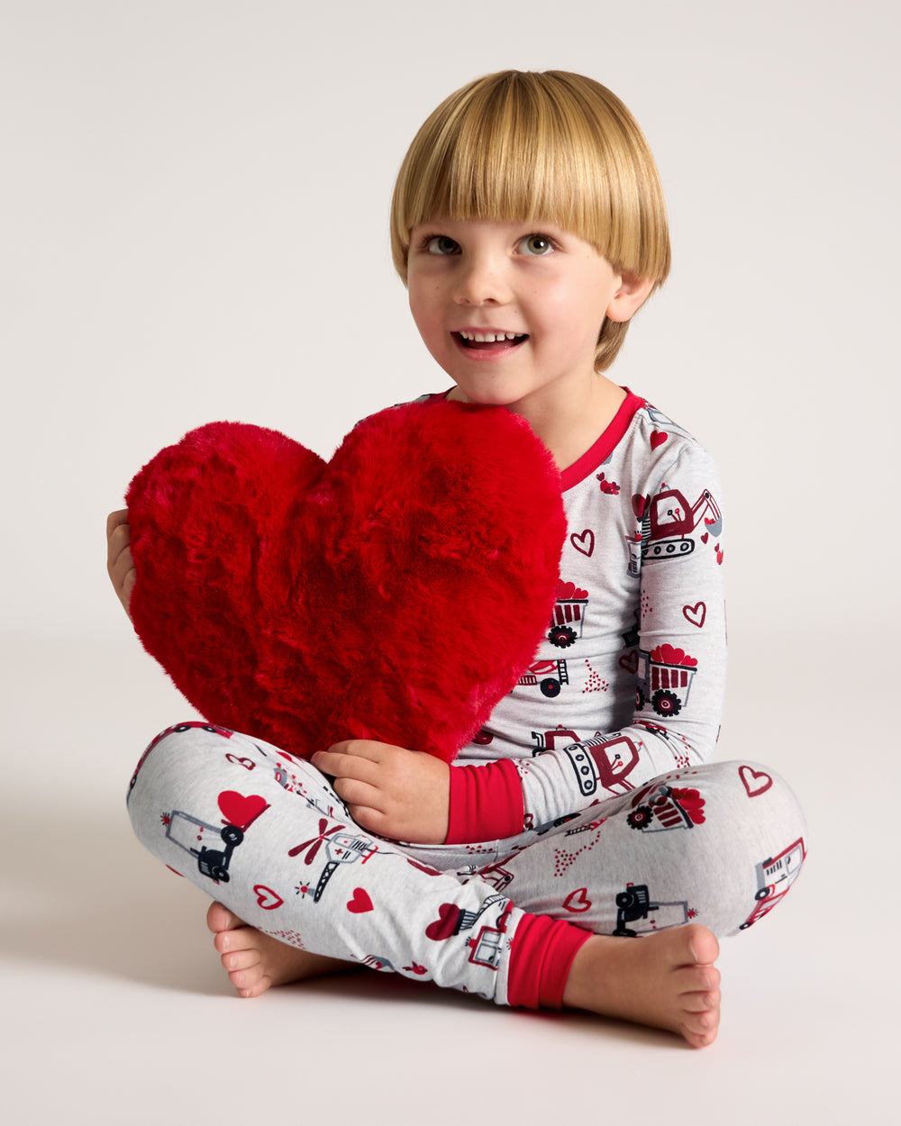 Boy wearing the Loads of Love Two-Piece Pajama Set holding a heart shaped pillow