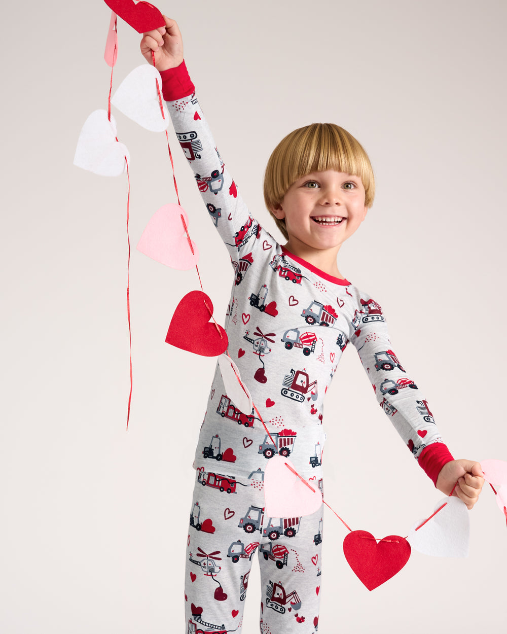 Boy wearing the Loads of Love Two-Piece Pajama Set holding a string of hearts 
