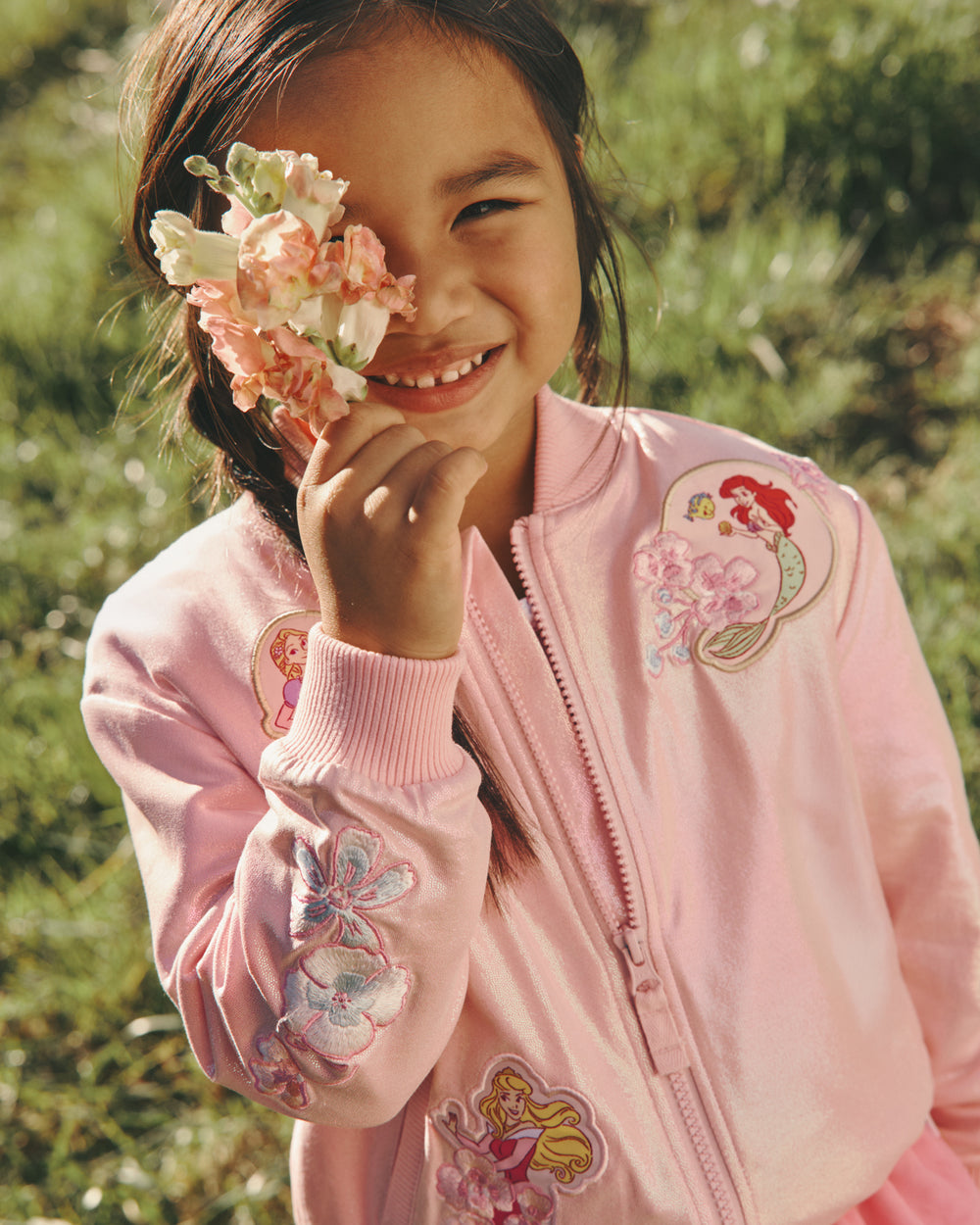 Girl posing with flowers wearing the Disney Princess Iridescent Varsity Jacket