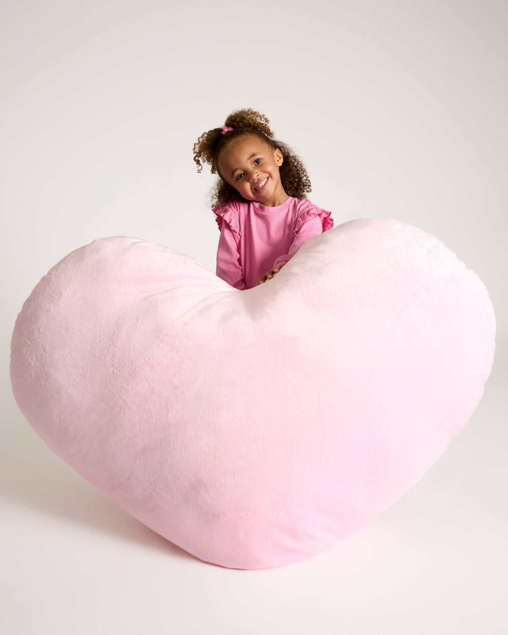 Girl wearing the Sweet Pink Ribbed Flutter Crewneck holding a large heart shaped pillow