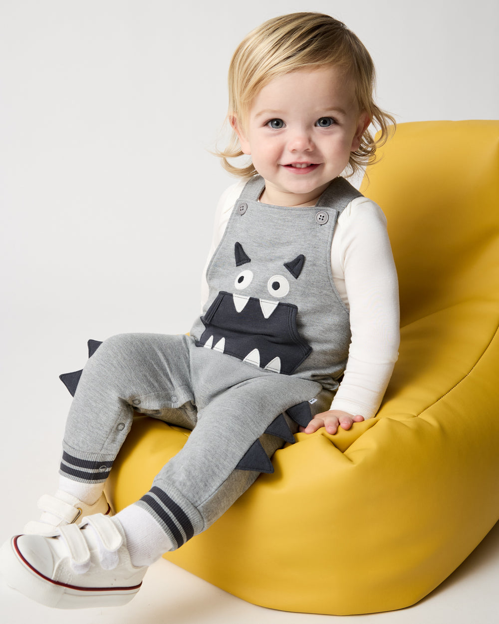 Child sitting on a yellow pouf wearing the Monster Overall