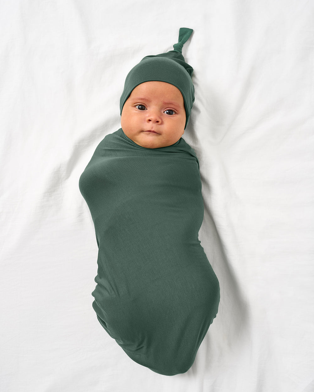 Aerial view of baby wearing the Grove Green Swaddle & Hat Set