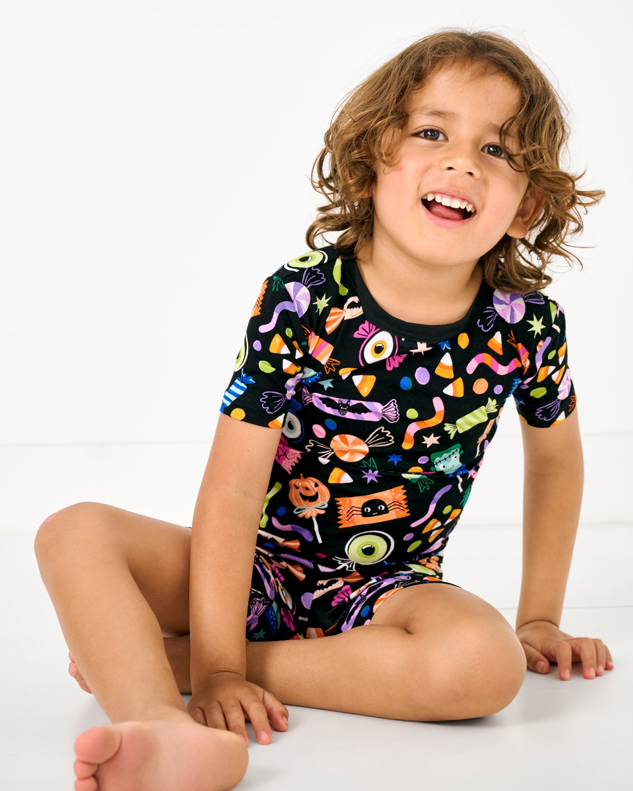 Sitting child wearing the Halloween Haul Two-Piece Short Sleeve & Shorts Pajama Set