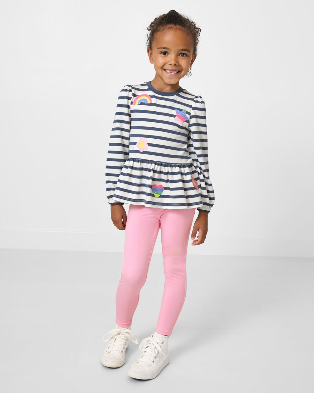 Standing girl wearing the Hazy Blue Stripe Puff Sleeve Peplum Top with pink leggings
