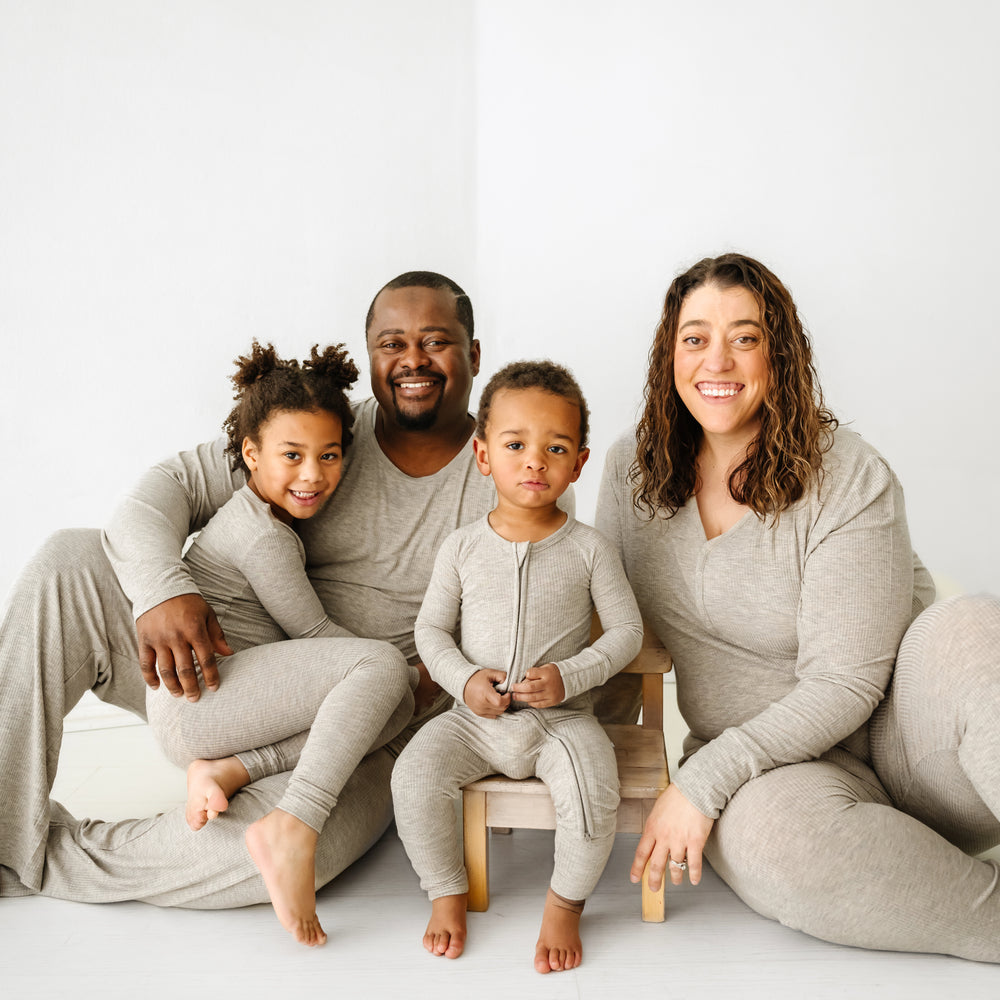Family of four wearing matching Heather Stone Ribbed pajama sets. Mom is wearing women's Heather Stone Ribbed pajama top and matching women's pj pants. Dad is wearing men's Heather Stone Ribbed pajama top and matching men's pj pants. Children are wearing matching two piece and zippy styles.