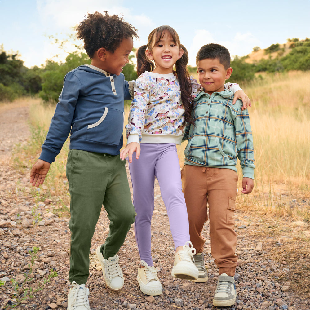 Three children outdoors walking together. Boy on the left is wearing the Vintage Navy Henley Hoodie and Olive Denim Joggers