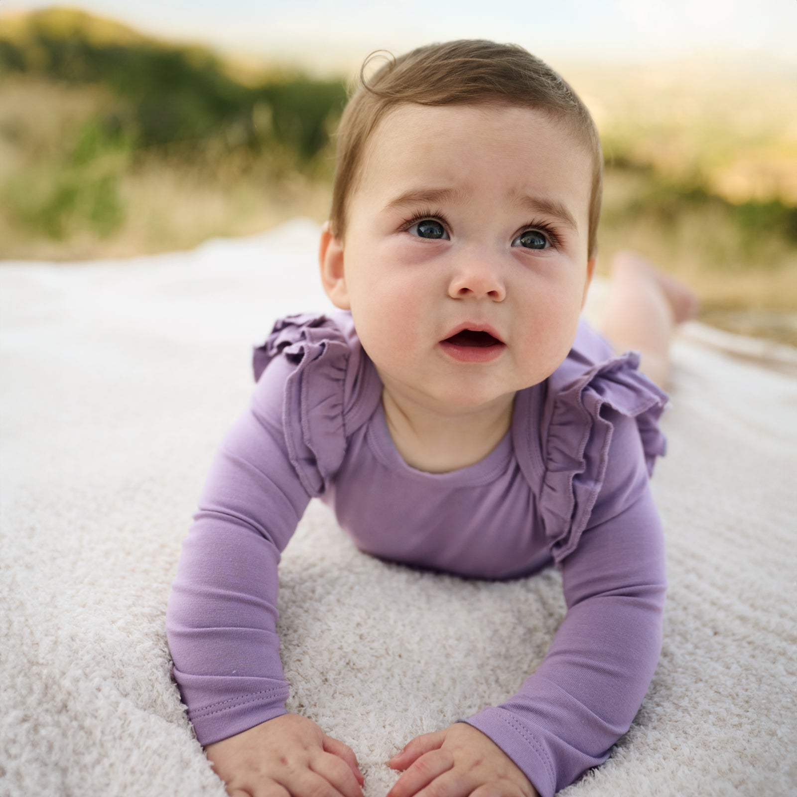 Close up image of baby laying down while in the Dusty Lavender Flutter Bodysuit