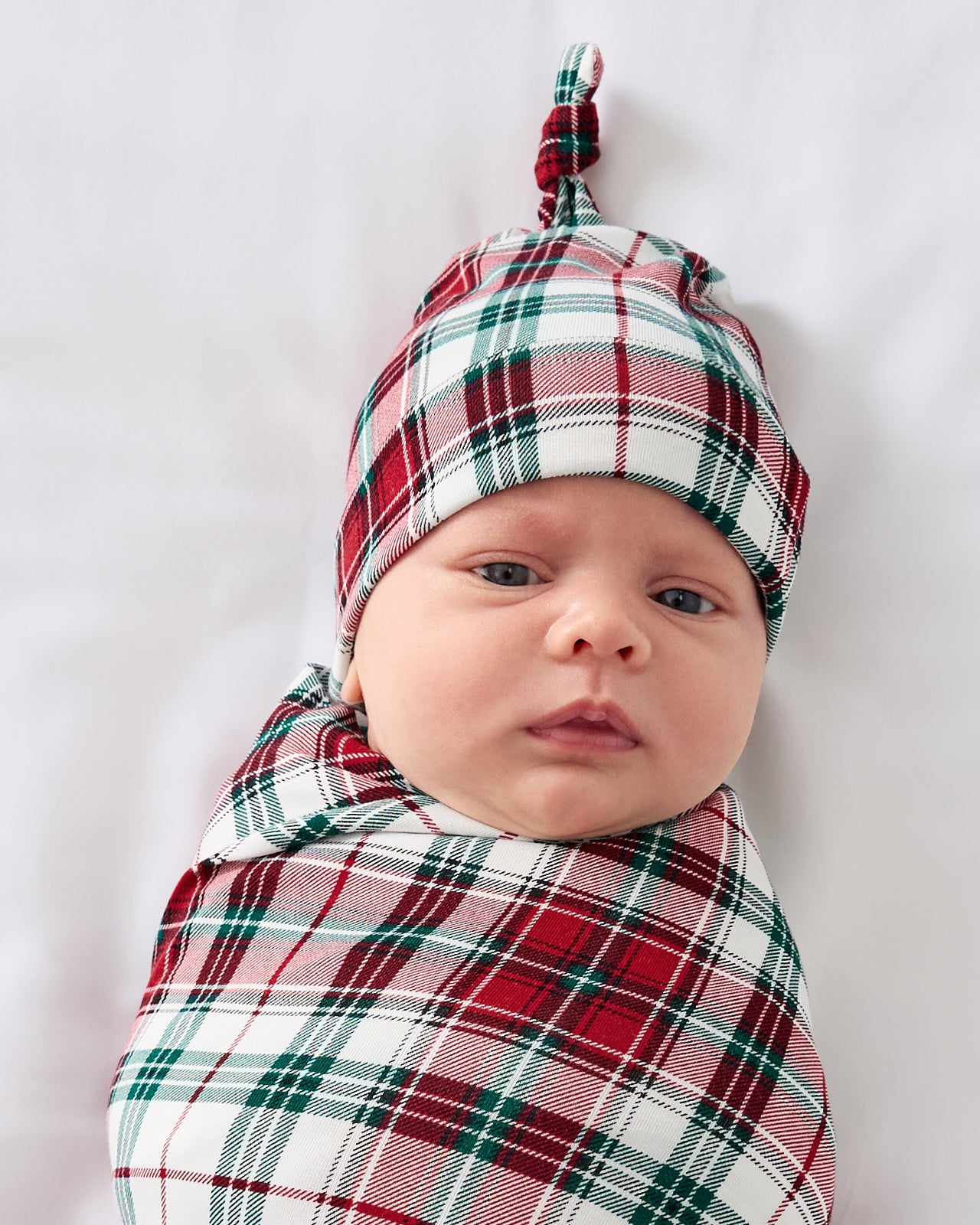 Close up of baby wearing the Holly Plaid Swaddle & Hat Set