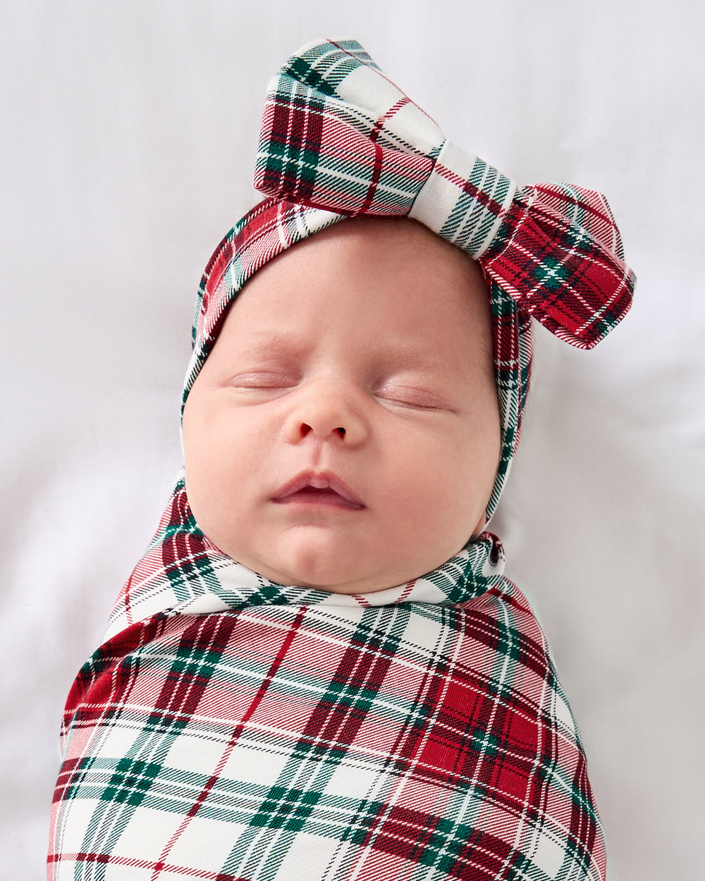 Close up of baby wearing the Holly Plaid Swaddle & Luxe Bow Headband Set
