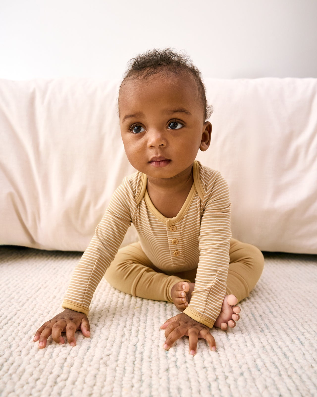 Sitting newborn wearing the Hazel Wood Stripe Henley Bodysuit with solid fold-over leggings