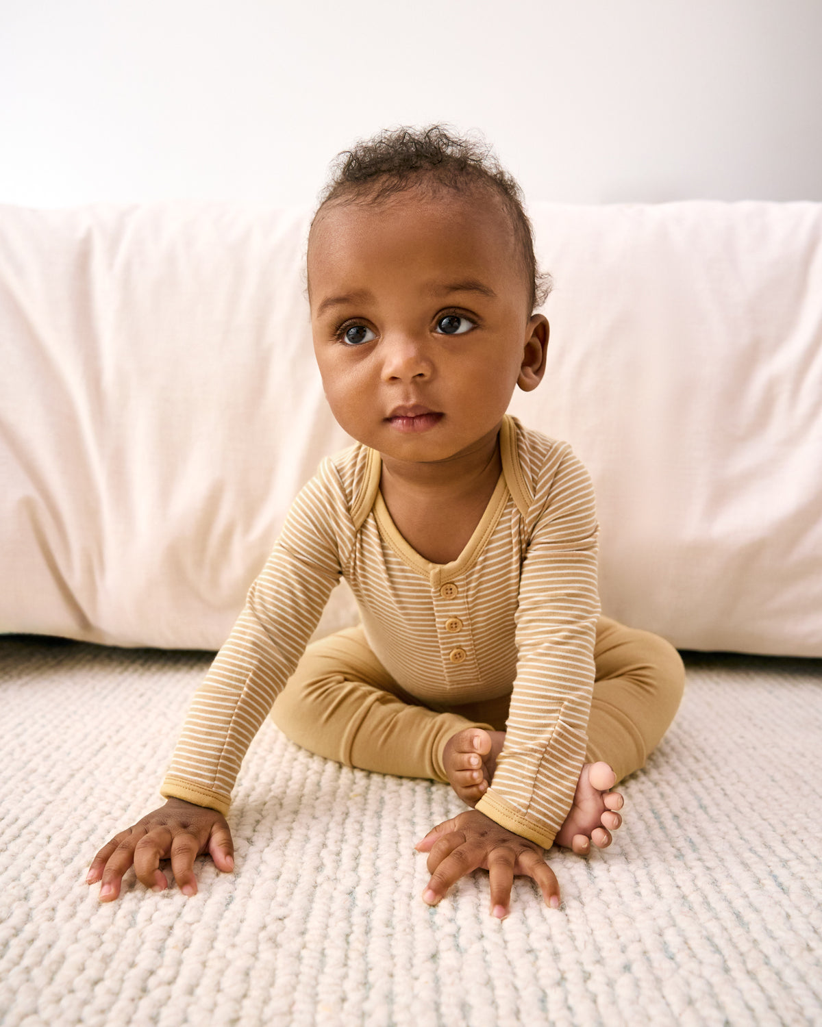 Sitting newborn wearing the Hazel Wood Stripe Henley Bodysuit with solid fold-over leggings
