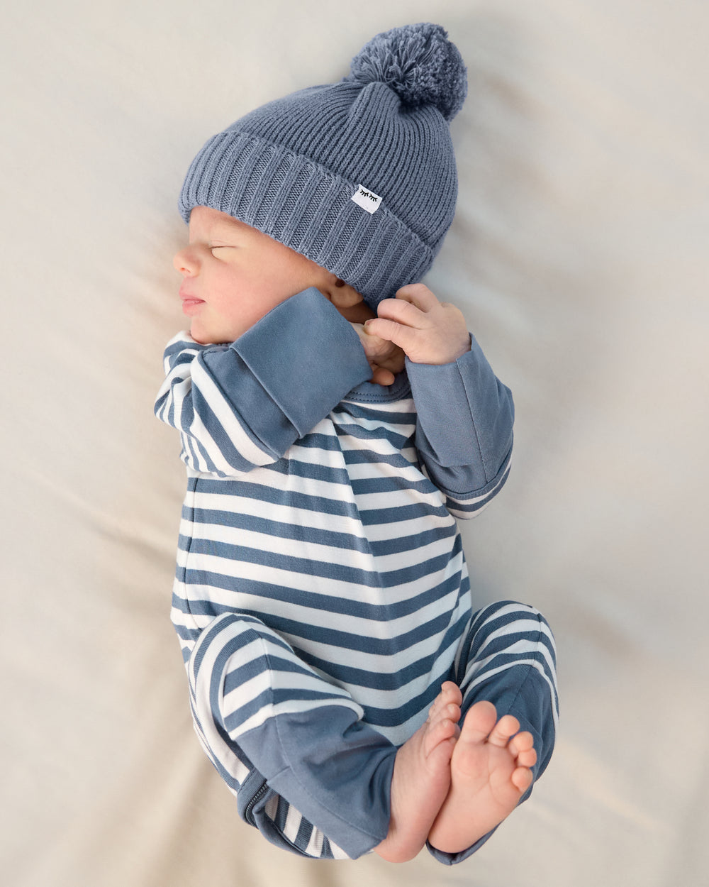 Newborn wearing the Hazy Blue Sweater Beanie Hat and a striped zippy