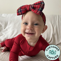 Customer capture of a child wearing a Holiday Plaid Luxe bow headband paired with a holiday red zippy