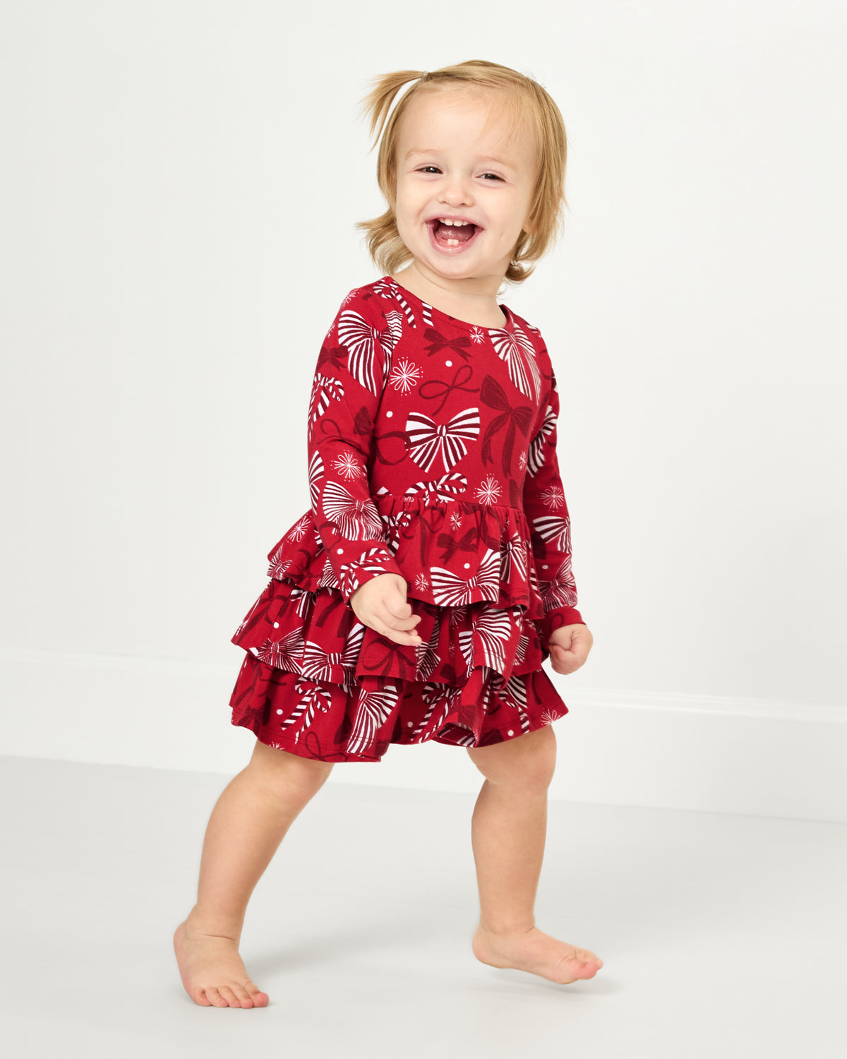 Walking toddler wearing the Holiday Bows Tiered Dress with Bloomer