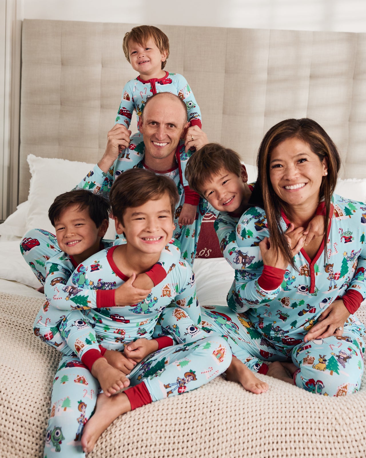 Family of six sitting on a bed wearing Disney & Pixar Christmas Village holiday pajamas