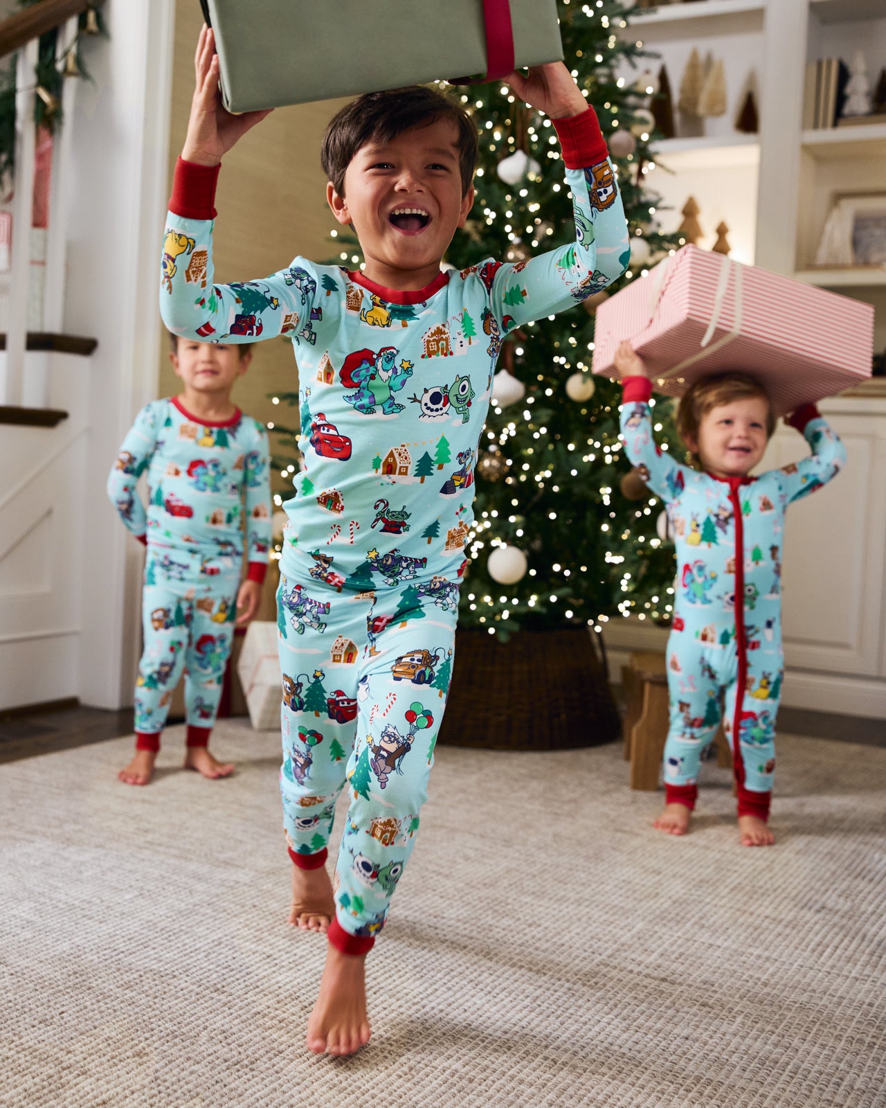 Three children holding Christmas gifts wearing Disney & Pixar Christmas Village pajamas