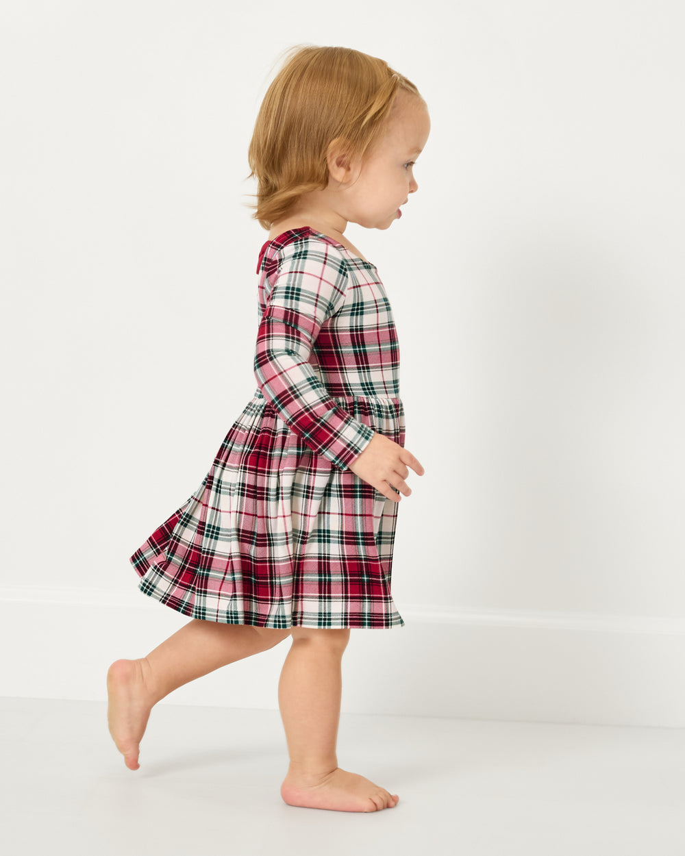 Walking toddler wearing the Holly Plaid Bow Back Skater Dress with Bodysuit