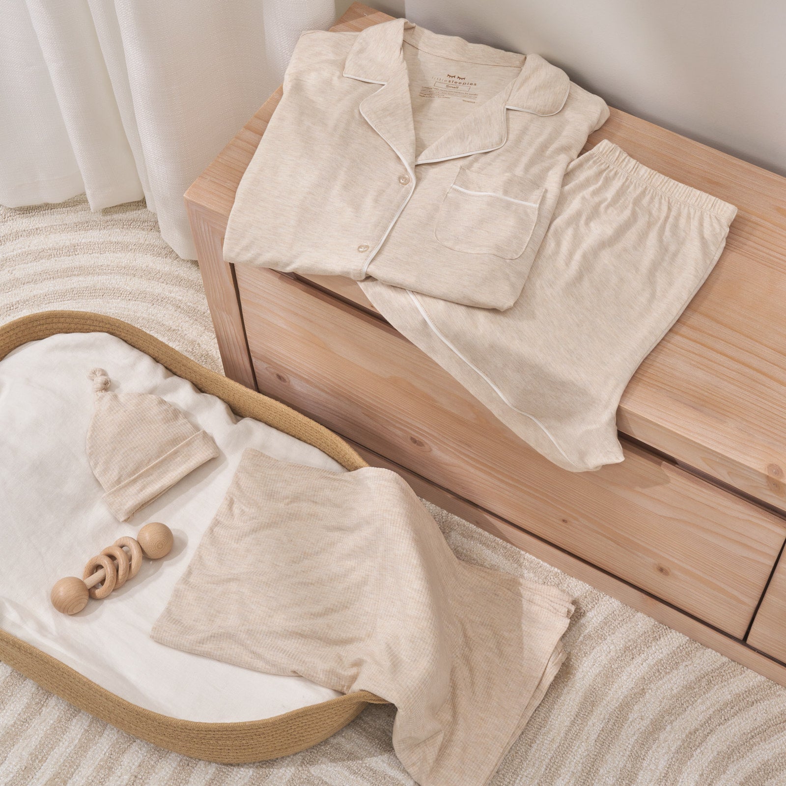 Still life photo of womens two piece pajama set on top of dresser with swaddle set with hat in a bassinet 