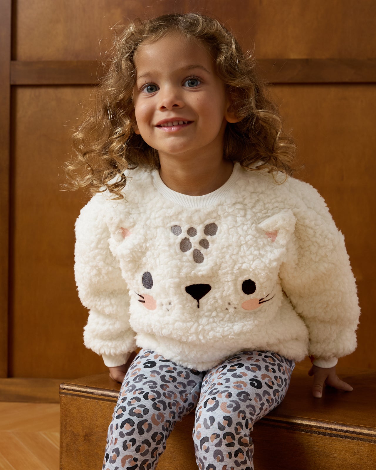 Girl sitting on a wooden box wearing the Leopard Drop Shoulder Crewneck 