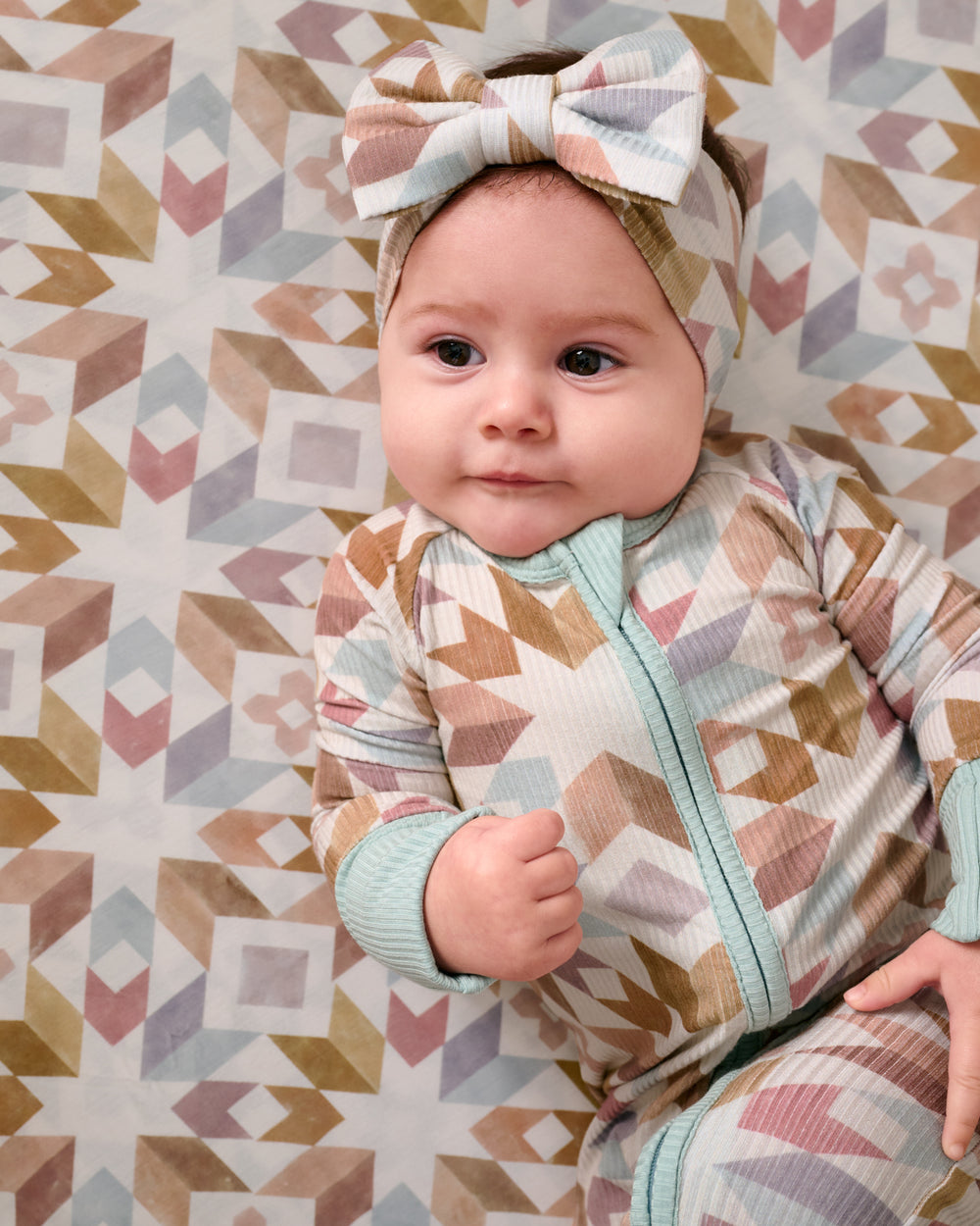 Close up of baby laying on the Baby sitting in a crib wearing the Kaleidoscope Dreams Zippy