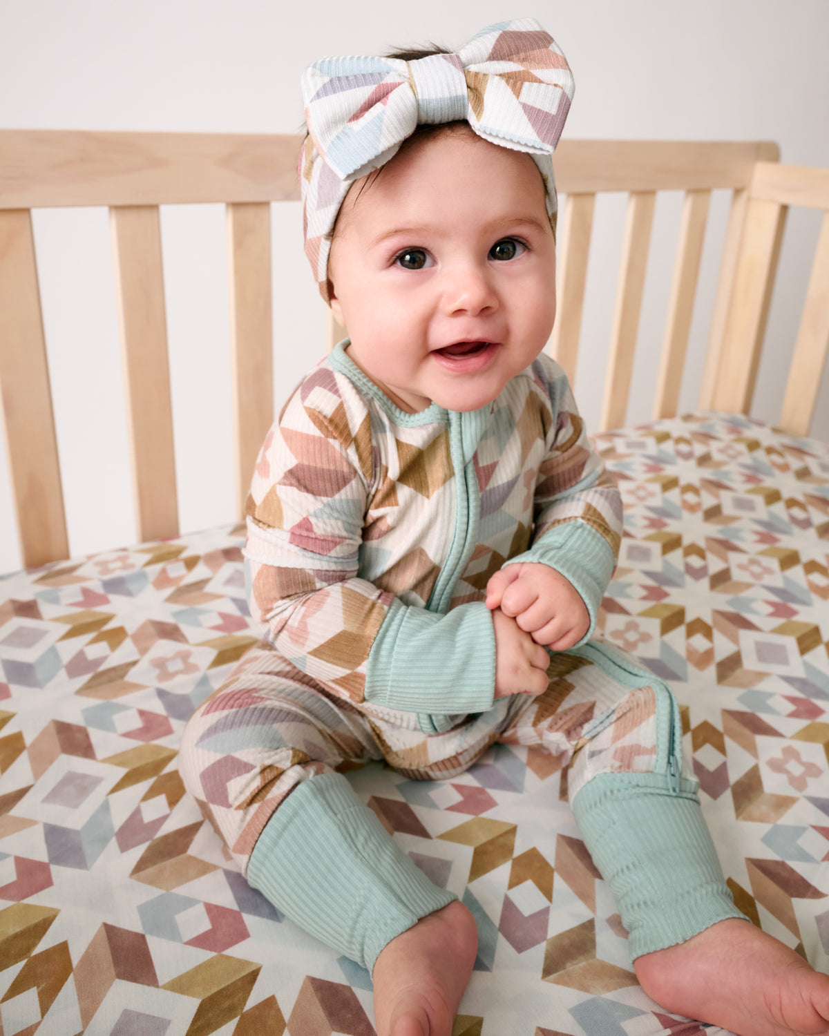 Baby sitting in a crib wearing the Kaleidoscope Dreams Zippy