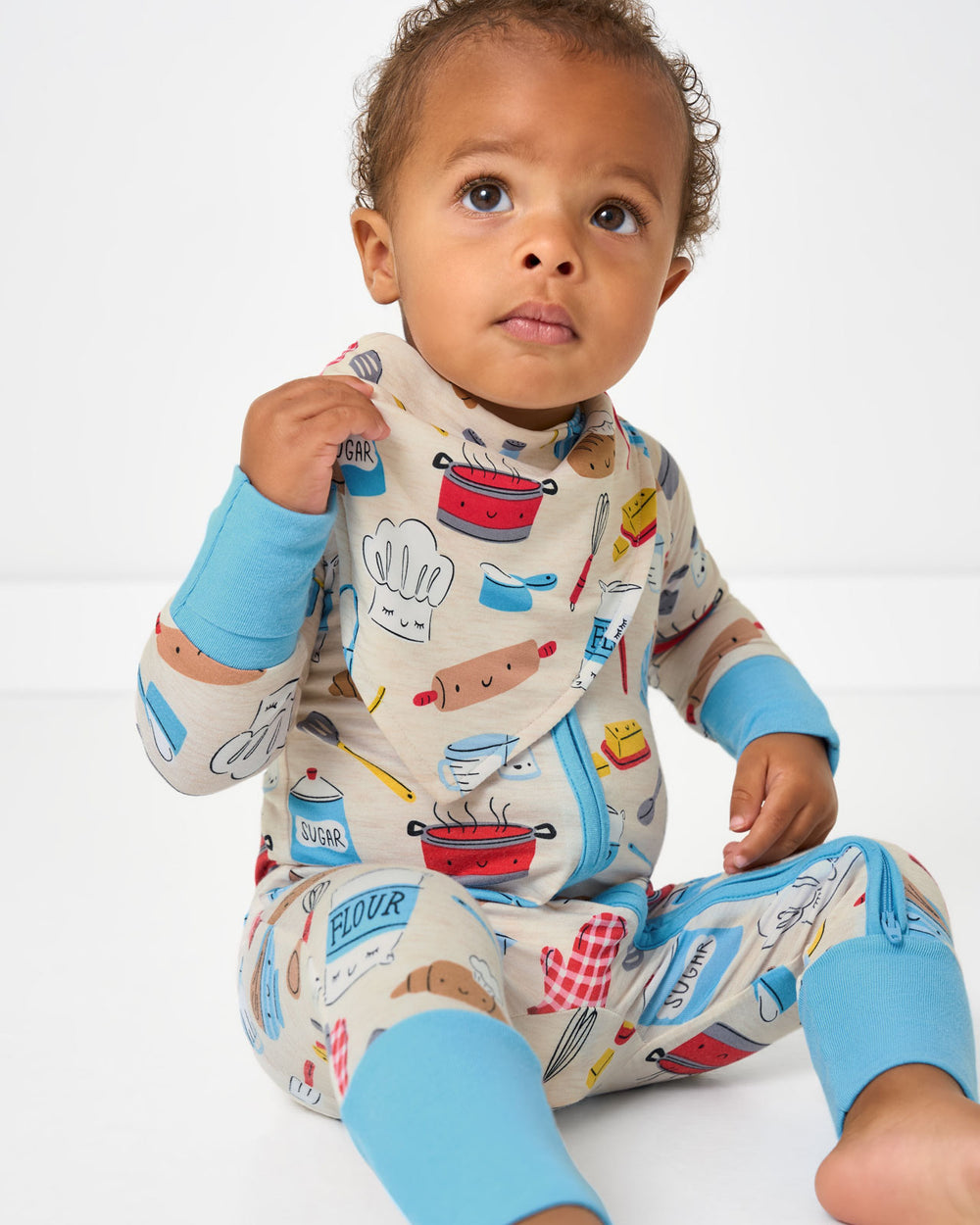 Sitting baby wearing the Little Chef Bandana Bib and Zippy
