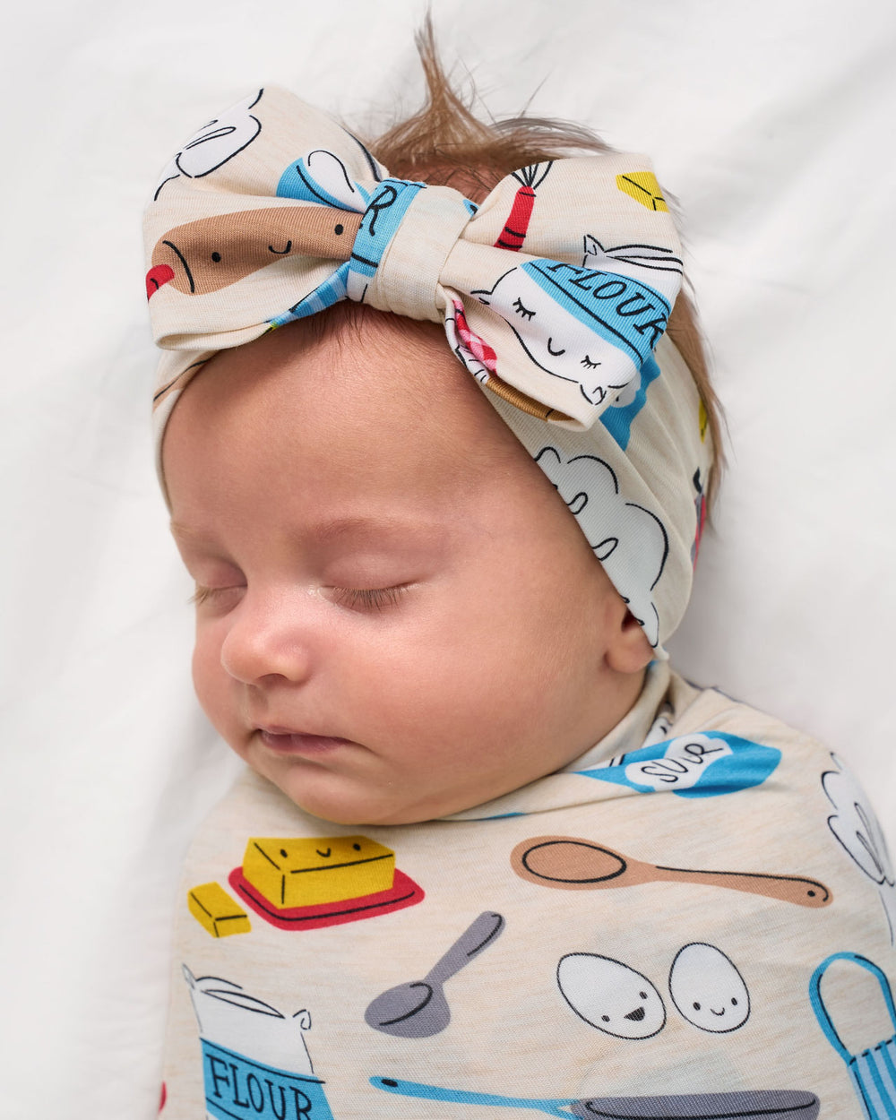 Close up of baby wrapped in the Little Chef Swaddle & Luxe Bow Headband Set