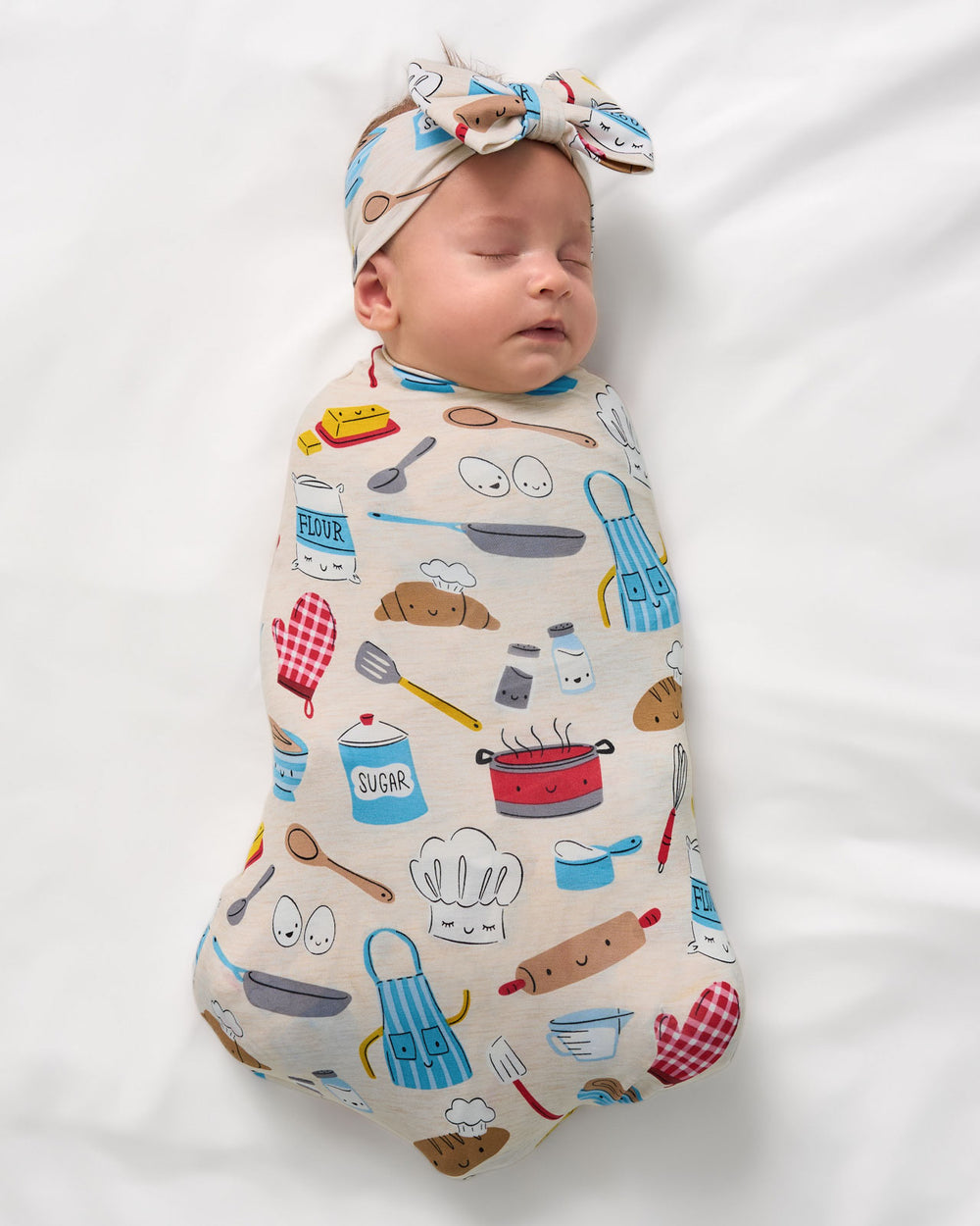 Aerial view of newborn swaddled in the Little Chef Swaddle & Luxe Bow Headband Set
