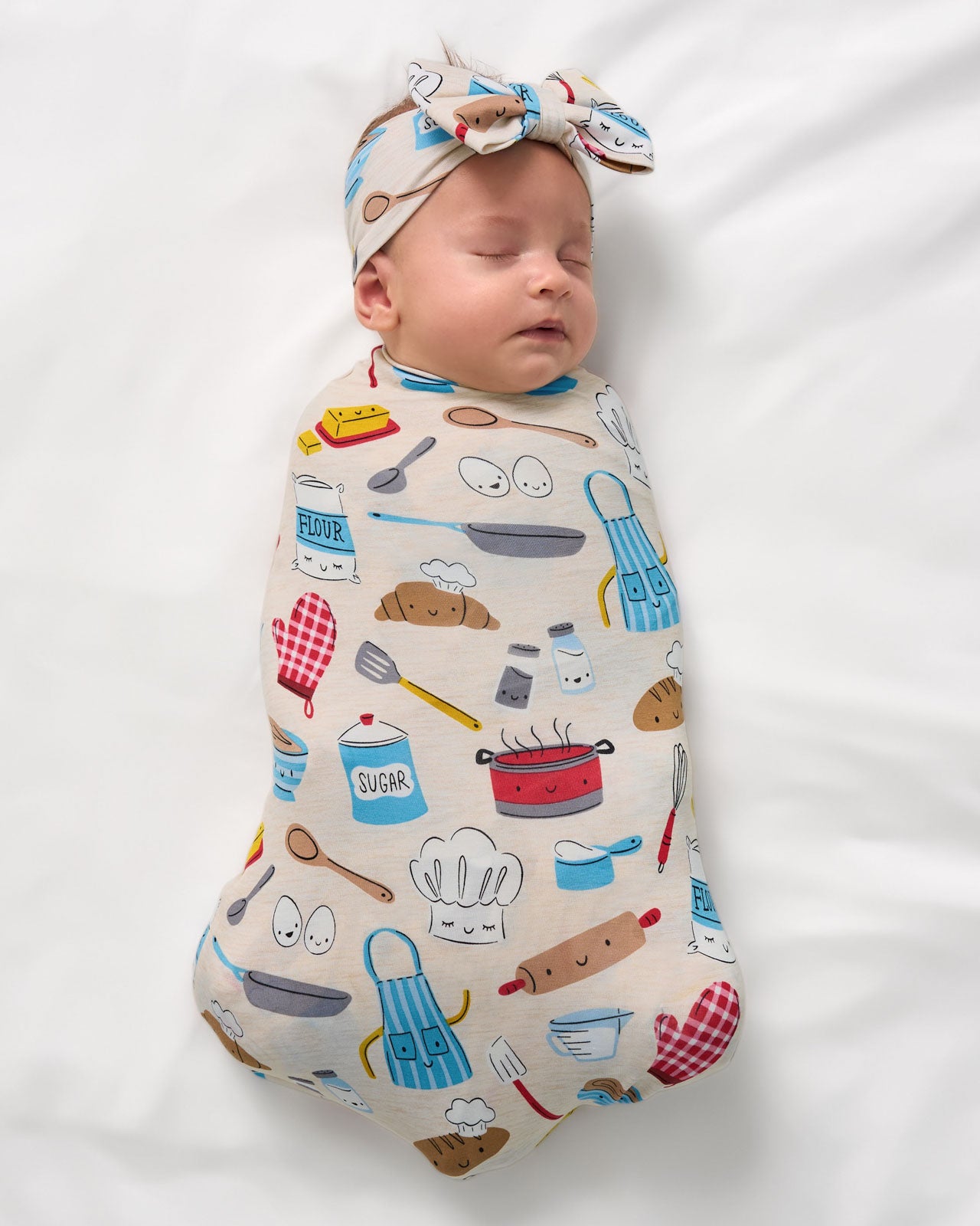 Aerial view of newborn swaddled in the Little Chef Swaddle & Luxe Bow Headband Set