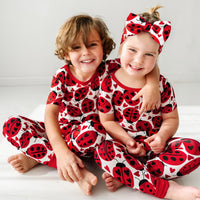 Two children sitting on the ground, one wearing a Love Bug printed luxe bow headband and both wearing matching Love Bug pajamas