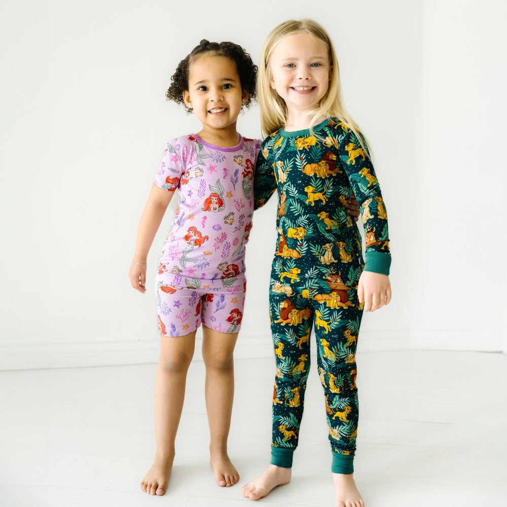 Two children posing together wearing Disney Part of Her World two piece shorts and short sleeve pajama set. The other child is wearing Disney's Simba's Sky two piece pajama set