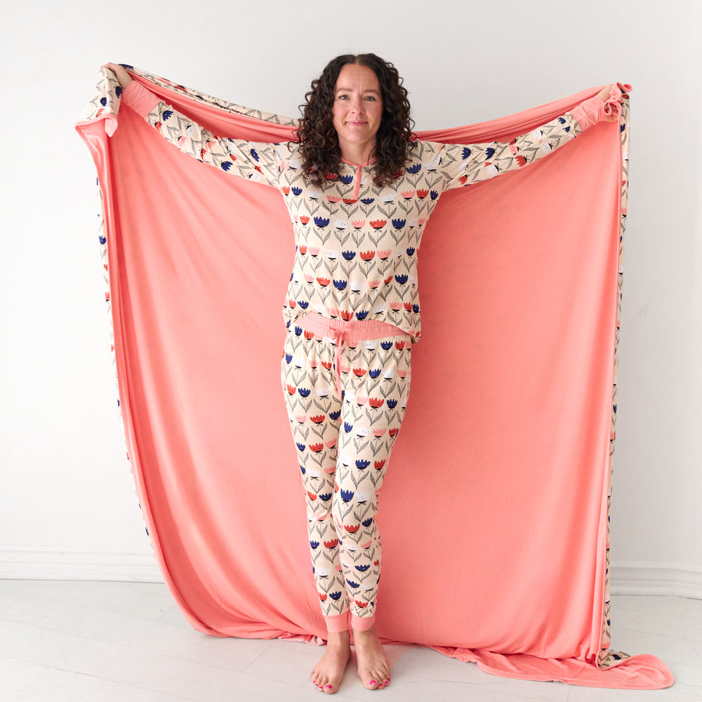 Woman holding out a Flower Friends oversized cloud blanket detailing the solid colored backing and wearing matching pajamas
