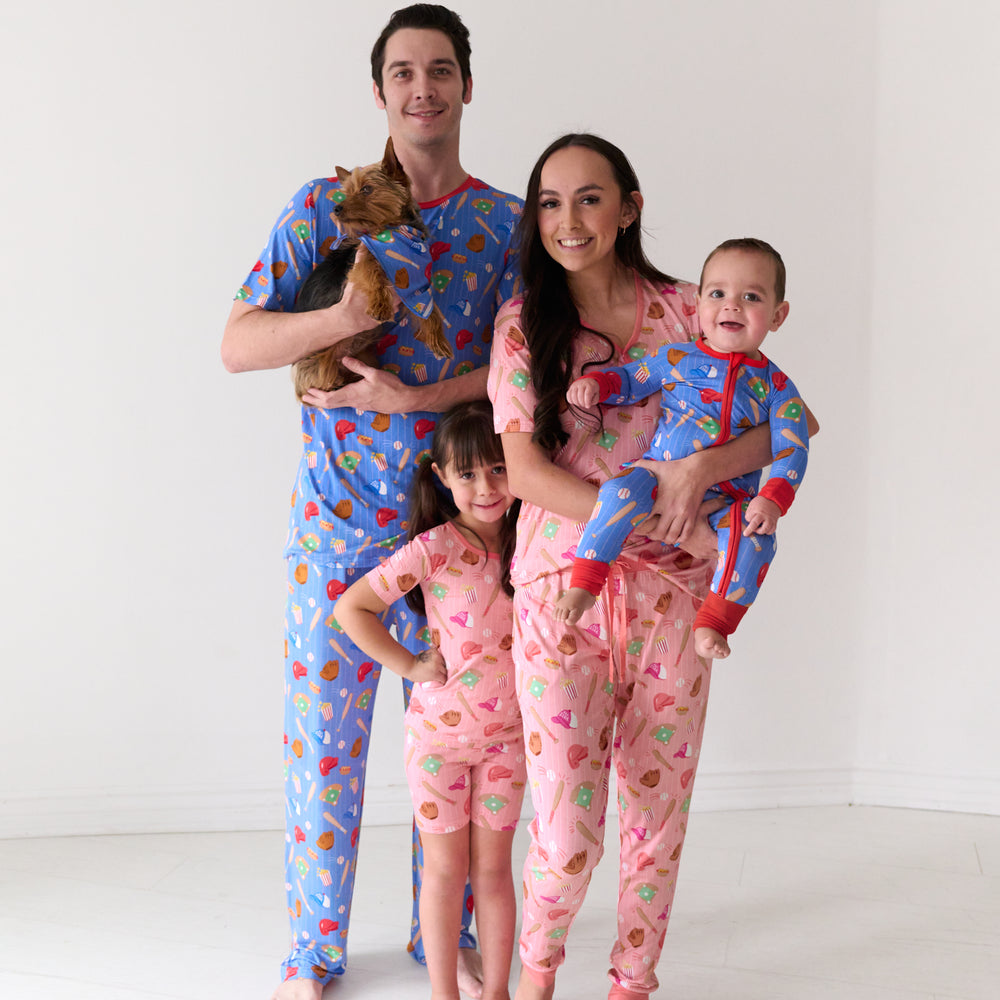 Family of four and their dog coordinating in All Stars printed pajama sets. Dad is wearing men's Blue All Stars pajama pants and matching men's pajama top. Mom is wearing women's pink All Stars pajama pants and matching women's pajama top. Kids are wearing Pink All Stars two piece short sleeve and shorts pajama set and a Blue All Stars zippy. Their dog is matching wearing a Blue All Stars pet bandana