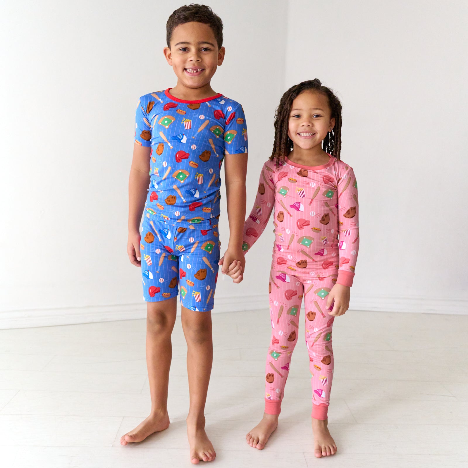 Two children holding hands wearing coordinating Pink and Blue All Stars pajama sets in short sleeve and shorts and two piece long sleeve pajama styles