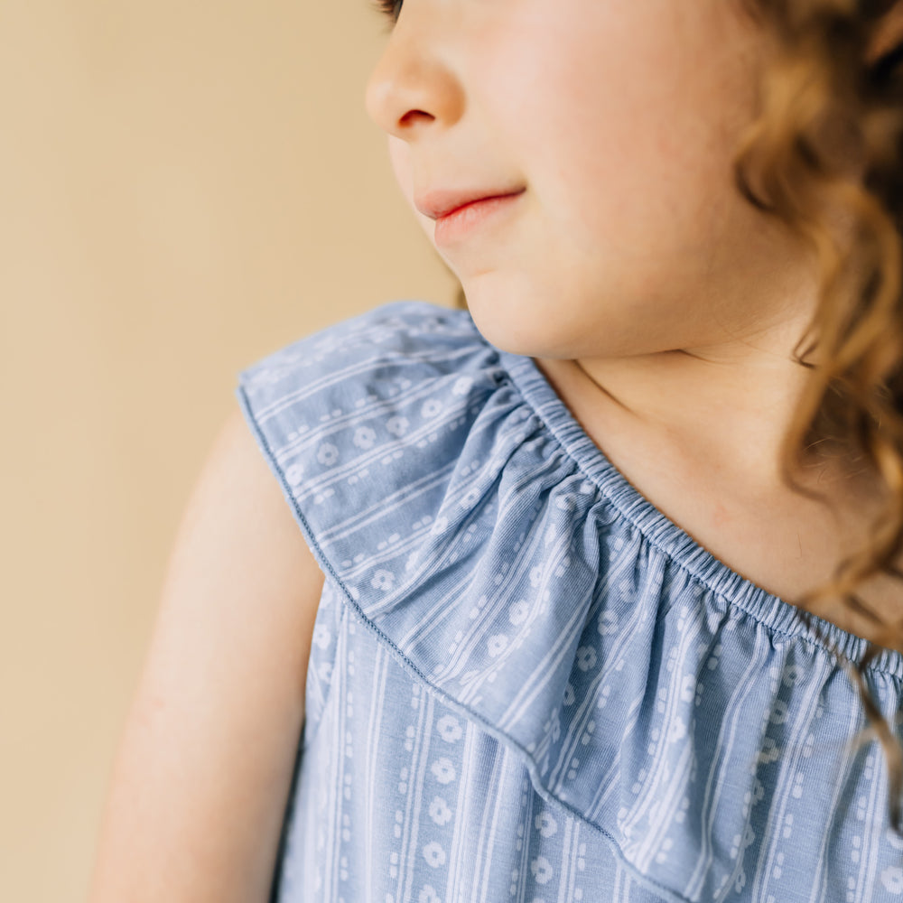 Close up image of a child wearing an Island stripe asymmetrical romper showing the ruffle shoulder