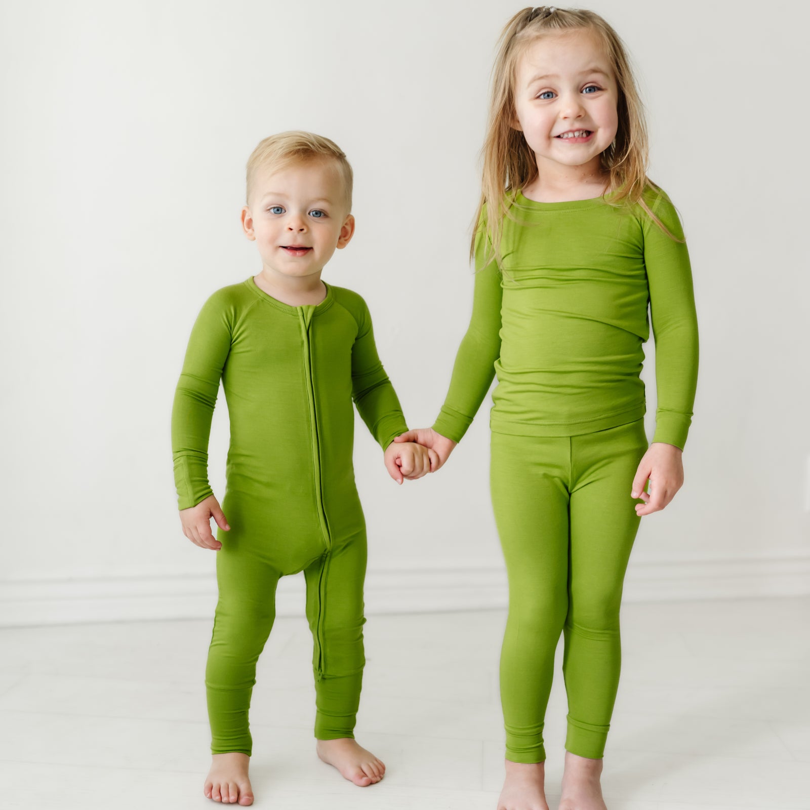 two children holding hands wearing matching Avocado pajamas in two piece and zippy styles