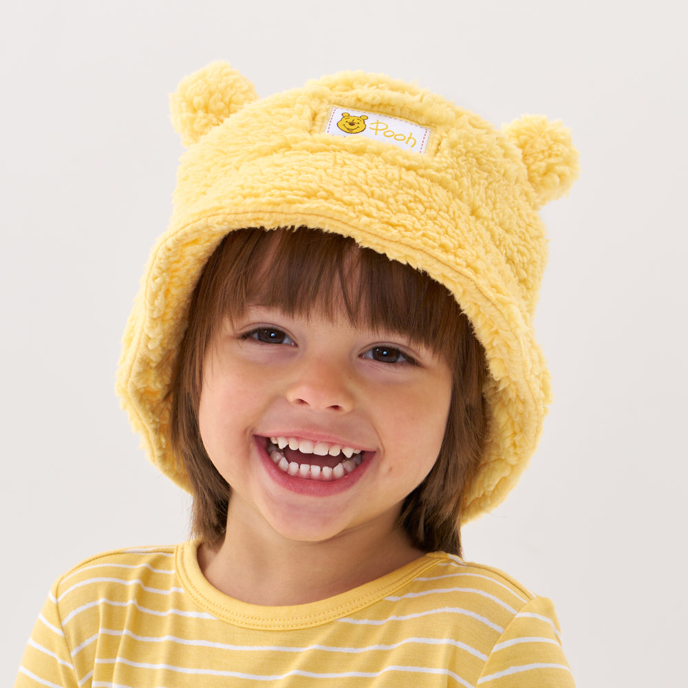 Click to see full screen - Close up image of a child wearing a Disney Winnie the Pooh sherpa bucket hat and coordinating graphic tee