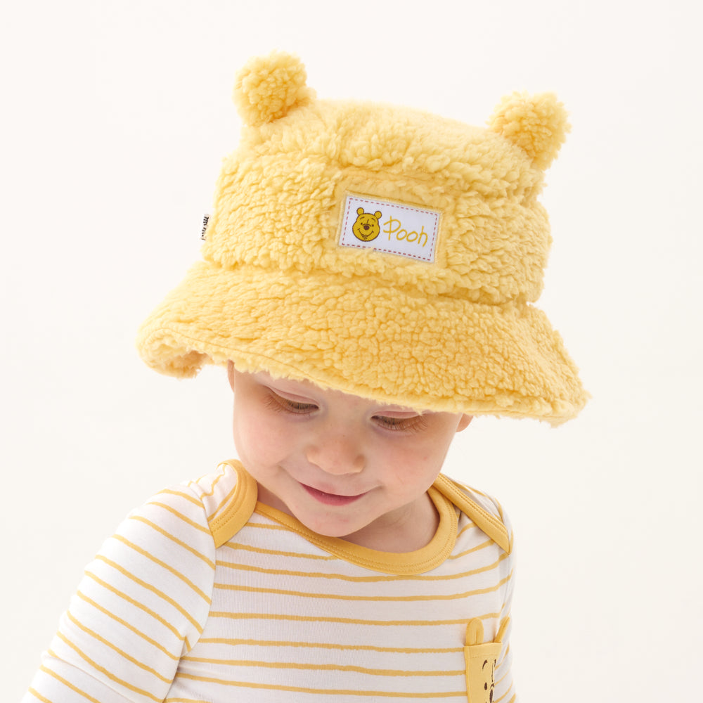 Click to see full screen - Child looking down wearing a Disney Winnie the Pooh sherpa bucket hat and coordinating graphic pocket bodysuit