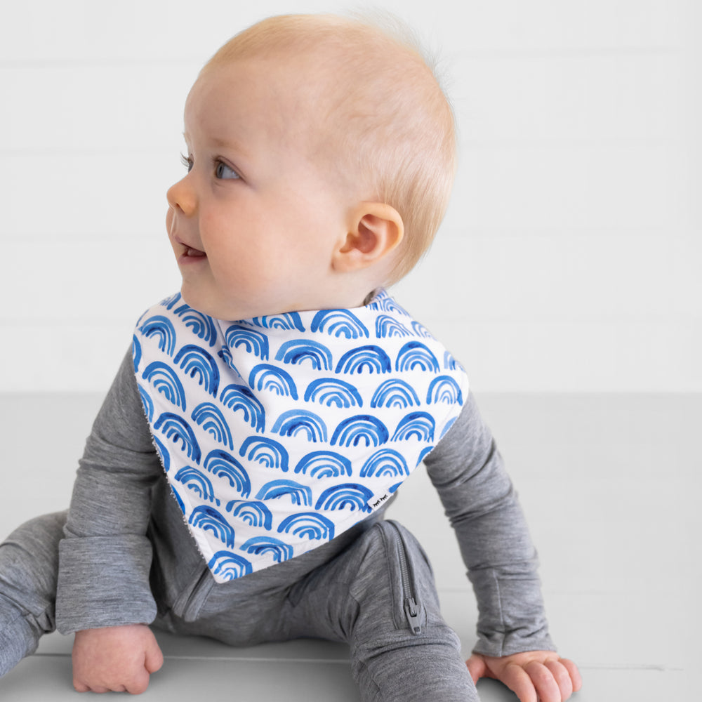 close up image of a child wearing a Blue Rainbows bandana bib over a heather gray zippy