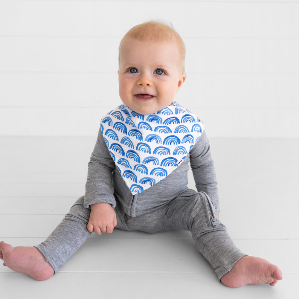 image of a child wearing a Blue Rainbows bandana bib over a heather gray zippy